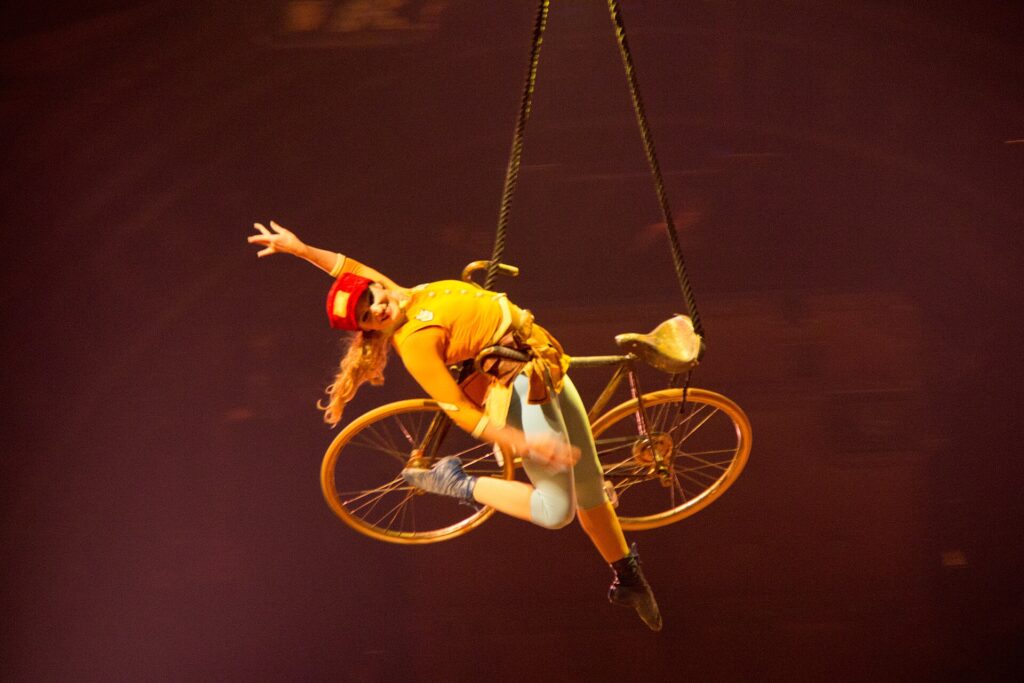Acróbata suspendida en el aire sobre una bicicleta en el espectáculo KURIOS de Cirque du Soleil