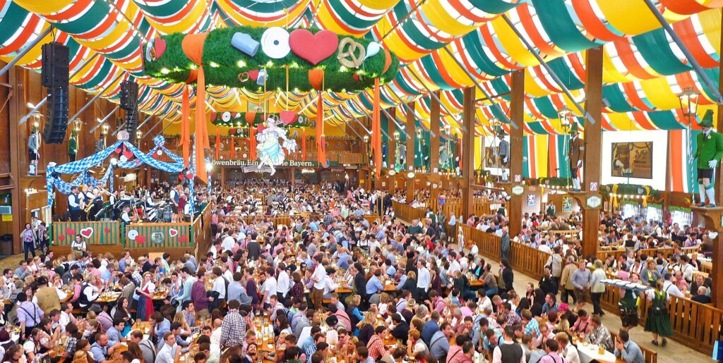 Interior de una carpa del Oktoberfest llena de gente en mesas corridas bajo un techo de tela de colores